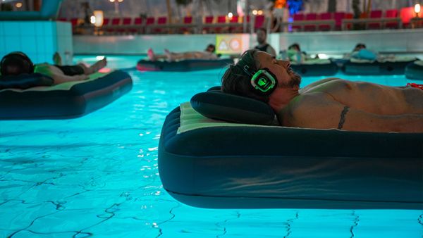 Mann liegt auf einer Luftmatratze und treibt auf dem Wasser und trägt Kopfhörer