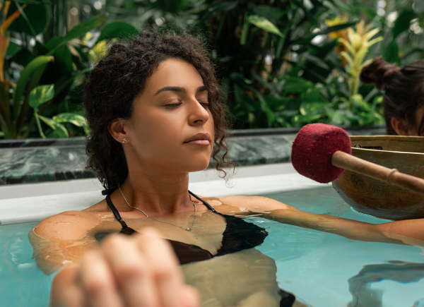 Frau im Wasser mit geschlossenen Augen und neben ihr eine Klangschale
