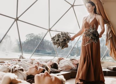 Frau wedelt mit Pirtszweigen über einer Gguppe von Menschen