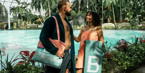 A man and a woman are standing by the lagoon at the Euskirchen thermal spa, wearing Bluphoria clothing, and laughing