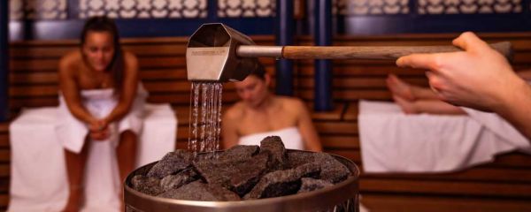 Saunaofen mit Saunakelle und zwei Frauen sitzen im Hintergrund