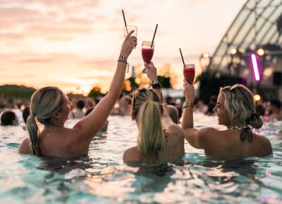 drei Frauen schwimmen im Pool und werfen die Hände nach oben