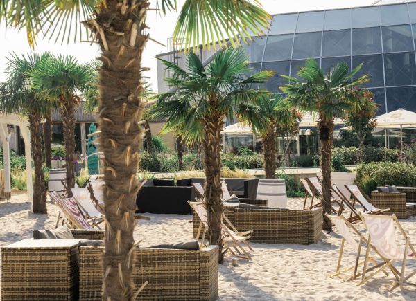 Strand, Palmen und Liegen neben einer Therme.
