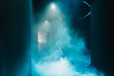A person walks through a room bathed in atmospheric blue light and filled with gentle mist in the Immersive Sky.