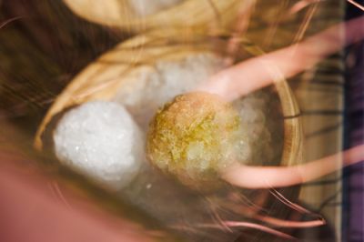 Nahaufnahme von zwei geformten Eisbällen mit Duftessenzen in einer Holzschale direkt über den erhitzten Steinen des Saunaofens.