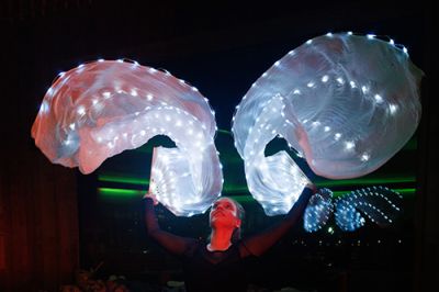 Eine Aufgusskünstlerin schwingt im abgedunkelten Raum zwei großflächig mit leuchtenden LED-Lichtern bestückte Fächertücher über ihrem Kopf.